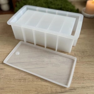 Può includere: Uno stampo in silicone trasparente con coperchio, progettato per realizzare più barre di sapone rettangolari o altri oggetti artigianali.