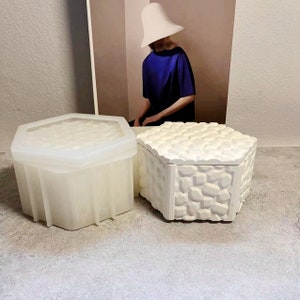 May include: Two white hexagonal boxes, one with a smooth surface and the other with a textured surface. Both boxes have lids.