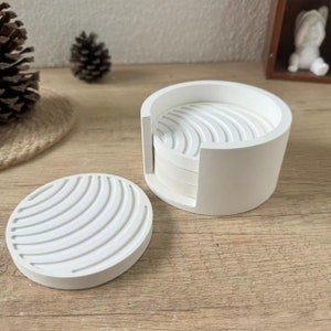 May include: Set of four white ceramic coasters with a wavy design, stacked in a white ceramic holder.