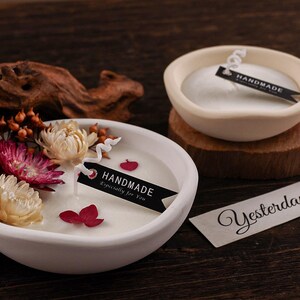 Puede incluir: Dos cuencos de cerámica blanca con velas y arreglos florales. Un cuenco tiene flores secas y una etiqueta que dice "HANDMADE Especially for You". El otro cuenco tiene una etiqueta que dice "HANDMADE". También hay una etiqueta que dice "Yesterday".