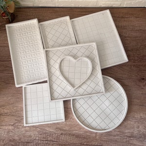 May include: Five white resin trays with different geometric patterns. The trays are square and round with a grid pattern and a heart shape.