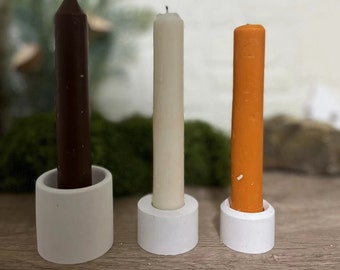 May include: Three candles in white, brown, and orange, each sitting in a white ceramic holder. The candles are on a wooden surface.