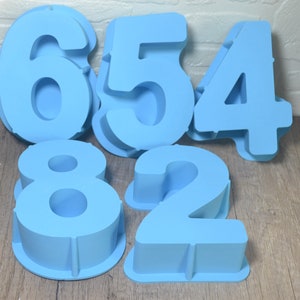 May include: Five blue silicone cake molds shaped like the numbers 6, 5, 4, 8, and 2.