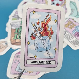 以下が含まれることがあります： 溶けかかった氷を剣が貫く漫画イラストのステッカー。ステッカーは薄い青色の背景で、下部に「ABOLISH ICE」の文字があります。
