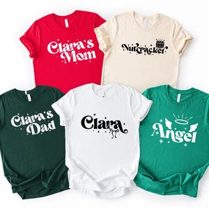 May include: Five short-sleeve crew neck t-shirts in red, cream, dark green, white, and bright green. The red shirt says Clara's Mom, cream says Nutcracker, dark green says Clara's Dad, white says Clara, and bright green says Angel with wings.
