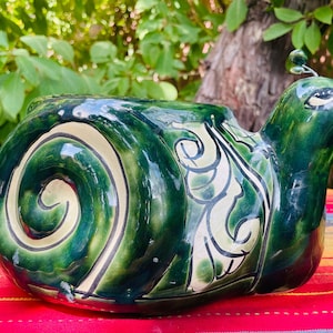 May include: Green and white ceramic snail planter with a detailed swirl pattern on the shell. The snail has a small antenna on its head.