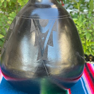 May include: Black ceramic vase with a geometric design. The vase has a rounded shape and a smooth, glossy finish.