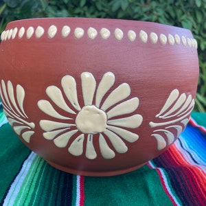 May include: Terracotta flower pot with white daisy designs. The pot has a brown glaze and a white rim with white dots.