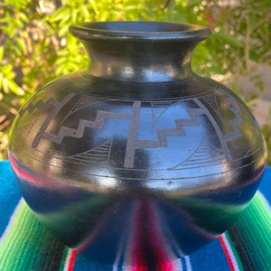May include: Black ceramic vase with a geometric design. The vase has a wide base and a narrow neck.