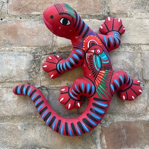May include: A red ceramic lizard with blue and green painted details. The lizard is painted with a stylized design and has a long tail.