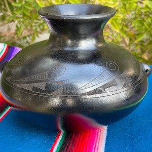 May include: Black ceramic vase with a geometric design. The vase has a wide base and a narrow neck.