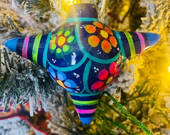 May include: A blue, green, pink, and yellow star-shaped Christmas ornament with a white string for hanging. The ornament is decorated with colorful dots and swirls.