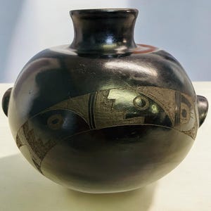 May include: Black ceramic vase with a geometric design. The vase has a round body and a narrow neck.