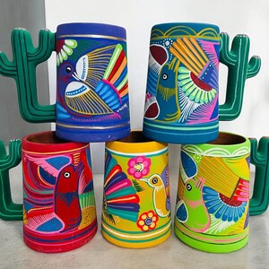 May include: Five colorful ceramic mugs with cactus-shaped handles. Each mug is hand-painted with vibrant colors and intricate designs featuring birds and flowers.