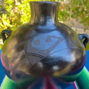 May include: Black ceramic vase with two handles and a geometric design. The vase has a glossy finish and is decorated with a carved pattern.