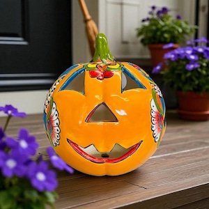 May include: A ceramic jack-o'-lantern with a bright orange finish, green stem, and colorful butterfly and floral accents. The pumpkin has triangular eyes and a wide, smiling mouth, perfect for Halloween decor.