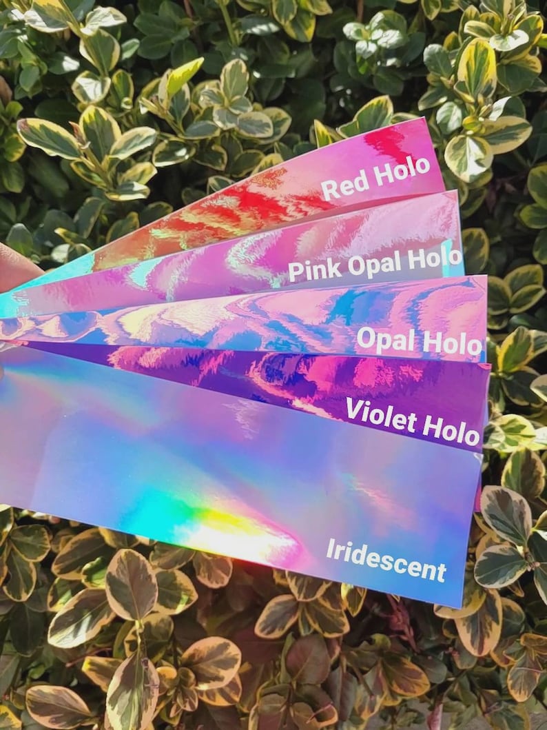 May include: A fan of five rectangular adhesive strips with holographic finishes in red, pink opal, opal, violet, and iridescent colors. Each strip features white text identifying the color: Red Holo, Pink Opal Holo, Opal Holo, Violet Holo, and Iridescent.