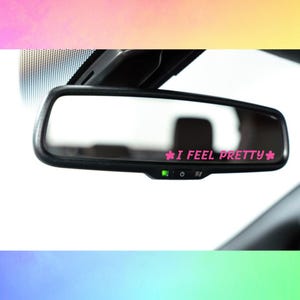 May include: A rearview mirror with a pink sticker that says "I feel pretty" with pink flower accents on either side of the text.
