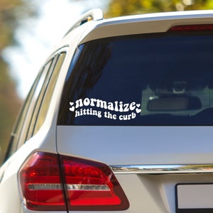 May include: White car with a sticker on the back window that says "normalize hitting the curb" with hearts on either side of the text.