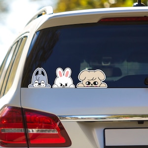 May include: Three cartoon animal stickers on a car window. A gray wolf, a white rabbit, and a brown dog are peeking over the top of the window. Each animal has a different expression on its face.