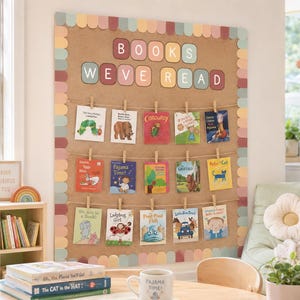 May include: A large rectangular cork notice board featuring a scalloped border in muted pastel tones. The text "BOOKS WE'VE READ" is displayed in individual colourful squares at the top. Fifteen children's book covers are clipped to three twine lines.