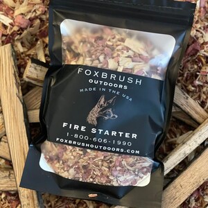 May include: A black package of fire starter from Foxbrush Outdoors, made in the USA. The package features a clear window showing the contents, with the words "Fire Starter" and a phone number. The background is wood shavings and small pieces of wood.