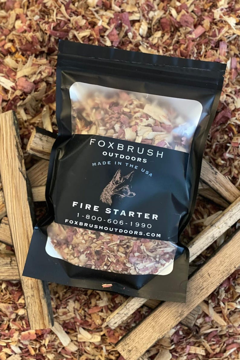 May include: A black package of fire starter from Foxbrush Outdoors, made in the USA. The package features a clear window showing the contents, with the words "Fire Starter" and a phone number. The background is wood shavings and small pieces of wood.
