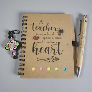 May include: A spiral-bound notebook with the text "A teacher takes a hand opens a mind and touches a heart." A matching pen and a charm with the word "teacher" are also present. The notebook has colorful sticky notes.
