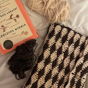 May include: A brown and cream crocheted bag with a button closure. The bag is made with a chevron pattern. Two balls of yarn, one brown and one cream, are also in the image.