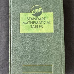 May include: A dark green hardcover book titled C.R.C. Standard Mathematical Tables. The cover features a textured finish with a light green rectangular panel containing the title in black text and a circular logo with the letters C.R.C. at the top.