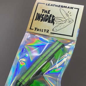 Op de afbeelding: Een groene Leatherman Free T2 multitool in een doorzichtige plastic zak met een zwart-wit label waarop "Leatherman The Insider Free T2" staat.