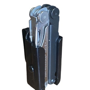 Könnte beinhalten: Ein schwarzes Leatherman Wave+ Multitool in einem schwarzen Kunststoffholster. Das Werkzeug ist geschlossen und das Holster hat eine Gürtelschlaufe.