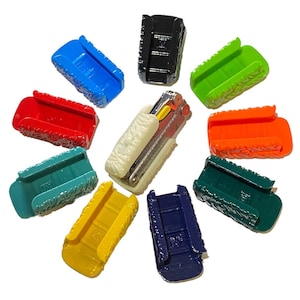 Könnte beinhalten: Eine Sammlung von zehn bunten Kunststoffhüllen, die für ein kleines Multitool konzipiert sind. Die Hüllen sind in einem Kreis um das Multitool angeordnet, das weiß mit silbernen Akzenten ist.