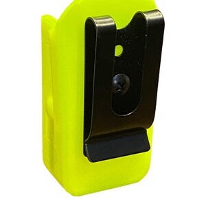 Puede incluir: Un clip de cintur&oacute;n de pl&aacute;stico amarillo brillante con un clip de metal negro. El clip est&aacute; dise&ntilde;ado para sujetar una linterna u otra herramienta peque&ntilde;a.