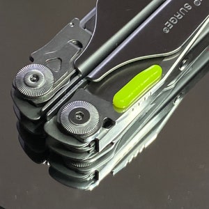 Könnte beinhalten: Ein silbernes Multitool mit grünem Akzent. Das Werkzeug verfügt über eine Vielzahl von Klingen und Werkzeugen, darunter ein Messer, eine Säge und einen Schraubendreher. Das Werkzeug ist geschlossen und zusammengeklappt.