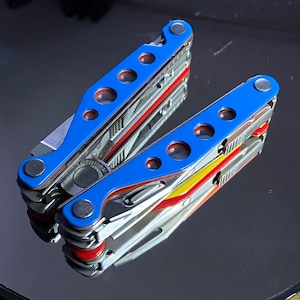 Könnte beinhalten: Ein blaues Multitool mit roten und gelben Akzenten. Das Werkzeug ist zusammengeklappt und verfügt über eine Vielzahl von Werkzeugen, darunter ein Messer, eine Zange und einen Schraubendreher.
