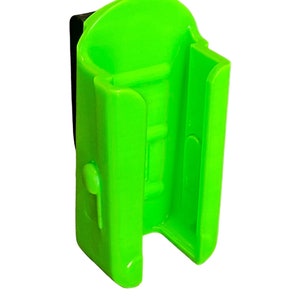 Puede incluir: Un soporte de luz de bicicleta de pl&aacute;stico verde brillante con un clip negro. El soporte tiene una ranura para una luz y un bot&oacute;n de liberaci&oacute;n en el lateral.