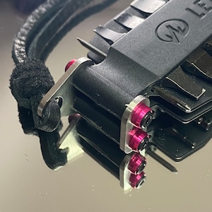 May include: A black multi-tool with a silver loop and a pink accent. The tool has a variety of blades and tools.