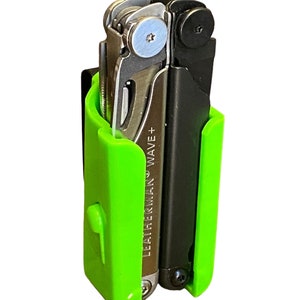 Könnte beinhalten: Ein grüner Multitool-Halter mit einem schwarzen Leatherman Wave+ Multitool im Inneren. Der Halter hat einen Clip an der Seite zum Befestigen an einem Gürtel oder einer Tasche.
