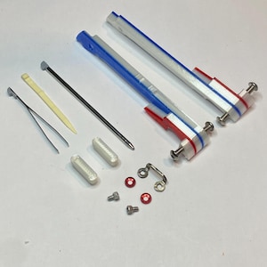 Puede incluir: Un conjunto de pequeñas piezas de plástico blanco, rojo y azul con tornillos de metal y otros accesorios. Las piezas son probablemente para un modelo o un juguete.
