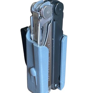 Könnte beinhalten: Ein graues und schwarzes Multitool mit einem Gürtelclip. Das Multitool befindet sich in einem grauen Kunststoffetui und hat den Text "LEATHERMAN WAVE+" auf der Seite.