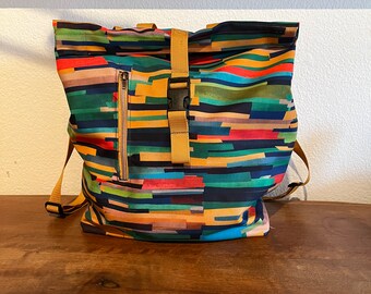 May include: A colorful, striped backpack with a yellow buckle and a zippered pocket. The backpack is made of a durable, water-resistant fabric.