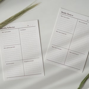 May include: Two printable planner pages with lined sections for weekly and monthly reflection. The pages are titled "Weekly Check-in" and "Monthly Reflection" with sections for "What I want to achieve", "What I want to remember", "My favorite moment", and "My good for next month".