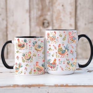 Puede incluir: Dos tazas de cer&aacute;mica blanca con asas y bordes negros. Las tazas est&aacute;n decoradas con ilustraciones coloridas de gallinas y motivos florales. Las tazas son de diferentes tama&ntilde;os, la m&aacute;s grande a la derecha.