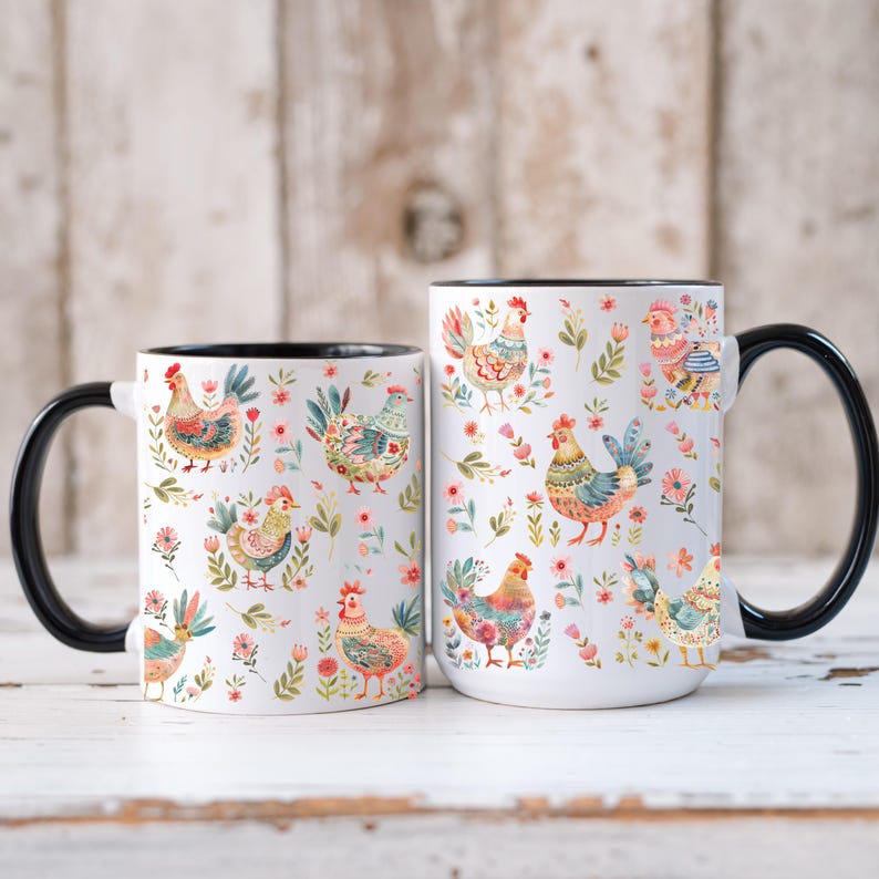 Puede incluir: Dos tazas de cer&aacute;mica blanca con asas y bordes negros. Las tazas est&aacute;n decoradas con ilustraciones coloridas de gallinas y motivos florales. Las tazas son de diferentes tama&ntilde;os, la m&aacute;s grande a la derecha.