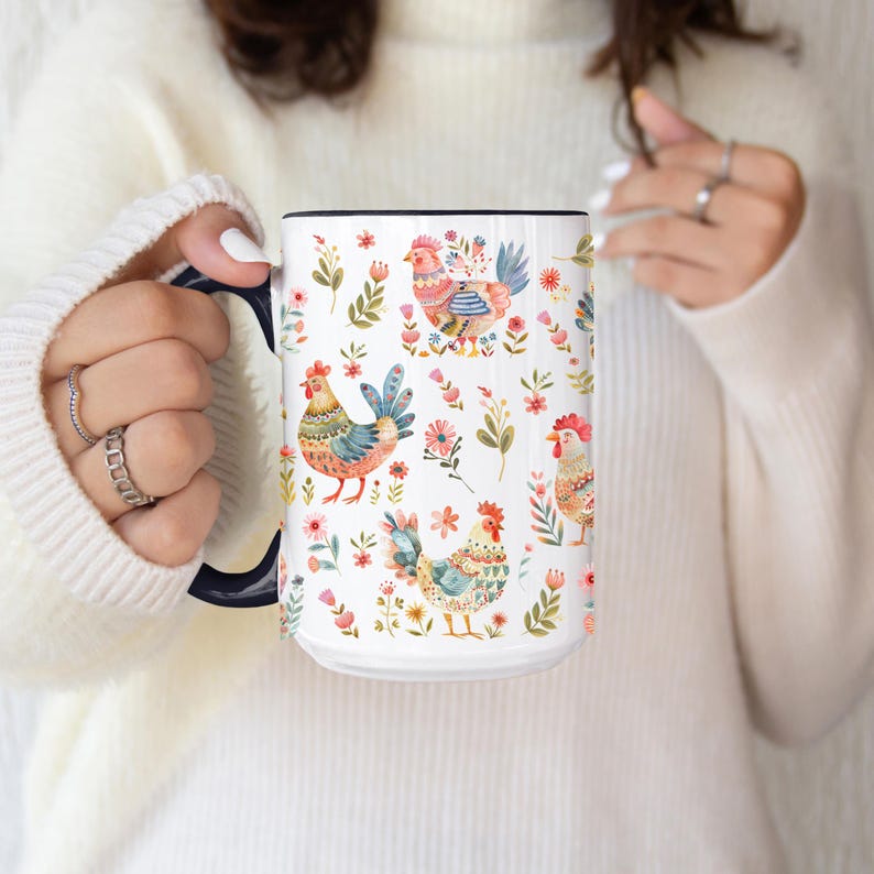Puede incluir: Taza de cer&aacute;mica blanca con interior y asa negros, adornada con un colorido estampado de gallinas, flores y follaje. El dise&ntilde;o presenta varias gallinas en colores vibrantes, rodeadas de elementos florales.