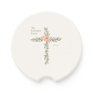 Puede incluir: Posavasos redondo blanco con un diseño de cruz floral. La cruz está hecha de hojas verdes y flores rosas. El texto "No Greater Love" y "John 15:13" está impreso en el posavasos.