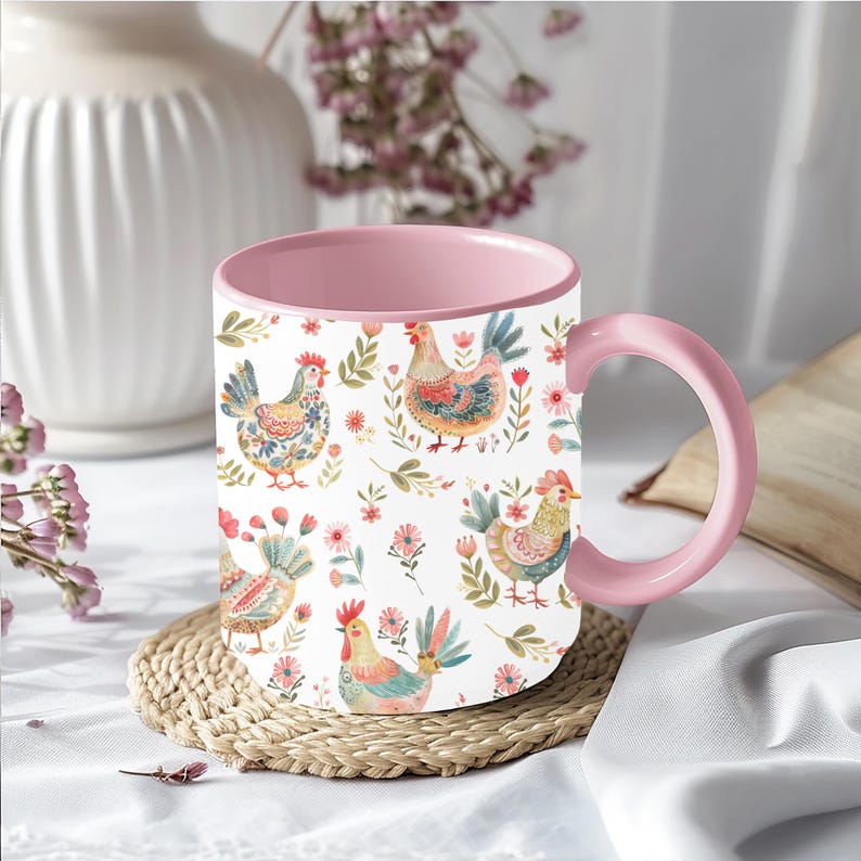 Puede incluir: Una taza de cer&aacute;mica blanca con interior y asa rosas. La taza presenta un patr&oacute;n repetido de gallinas, flores y hojas coloridas. La taza est&aacute; sobre un posavasos tejido.