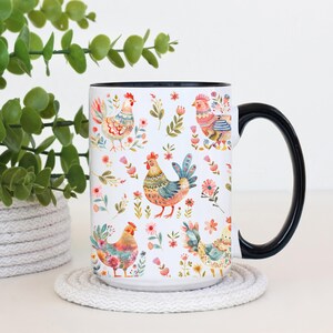 Puede incluir: Taza de cer&aacute;mica blanca con asa y borde negros, con un colorido estampado de gallos y flores. El dise&ntilde;o incluye varios gallos en diferentes poses, rodeados de flores rosas y naranjas y hojas verdes. La taza est&aacute; sobre un posavasos blanco.