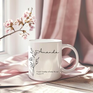 Può includere: Una tazza in ceramica bianca con un design floreale nero e il nome "Amanda" stampato su di essa. La tazza ha anche la citazione "Una dolce amicizia rinfresca l'anima" e "Proverbi 27:9" stampati su di essa.